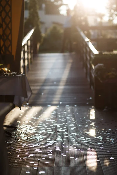 Wooden floor with colourful confetti on it. Blurred wooden bridge and a man, standing on it at the background. Wedding ceremony concept. — Stock Photo, Image