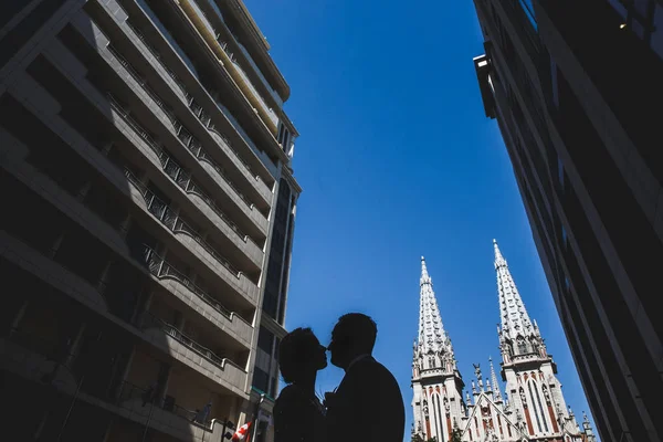 Silhuette van het jonge gehuwde paar in een romantische stads atmosfeer. Gotische kapel op de achtergrond. — Stockfoto