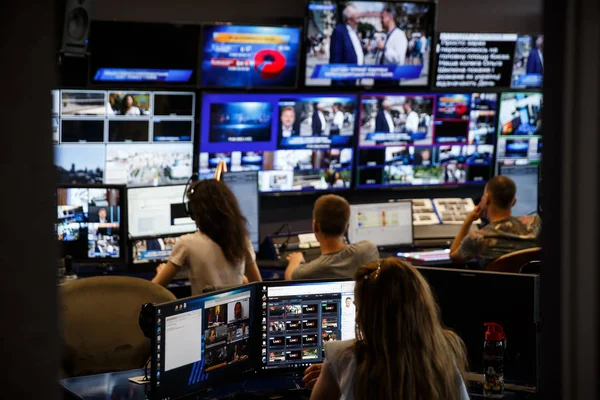 Bilgisayar üzerinde çalışan televizyon operatörü. Arka planda büyük yayın merkezi.