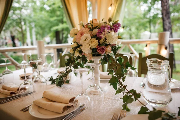 Ein großer Strauß und jede Menge Besteck stehen auf dem Tisch. Restaurant-Terrasse im Hintergrund. — Stockfoto