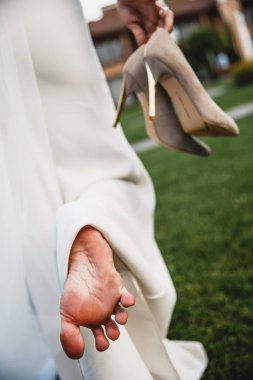 Bir gelin çimenlerin üstünde yalınayak onun yüksek topuklu onun sağ elinde tutarak yürüyor.