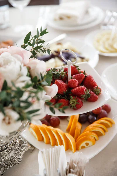A bunch of a plates with a food are standing on a table. Strawberries and the flower bouquet at the foreground. — Stock Photo, Image