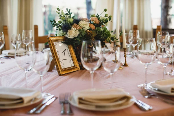 A lots of cutlery and some wineglasses are standing on the table. There is a flower bouquet at the middle of the table. — Stock Photo, Image