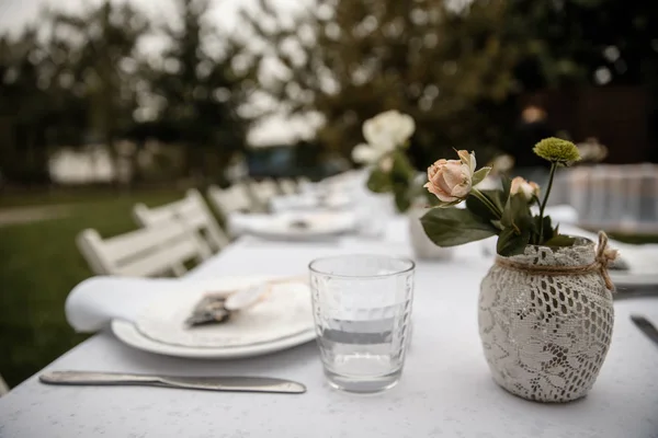 Some cutlery and a flowers in a pot are standing on the table. A park is on the background. — Stock Photo, Image