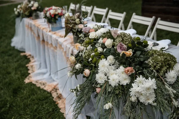 Ένα μεγάλο τραπέζι με πολλές καρέκλες παράλληλα με αυτό και μια δέσμη των λουλουδιών και τα μαχαιροπήρουνα σε αυτό. — Φωτογραφία Αρχείου