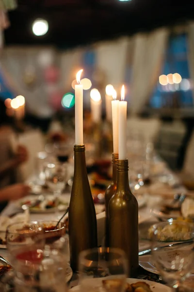 Three candles standing in the middle of a table alongside with a lots of food and cutlery. — Stock Photo, Image