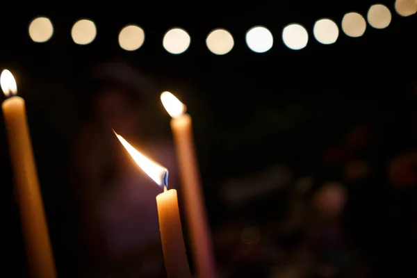 Três velas acesas estão no escuro. Uma guirlanda enevoada está no fundo . — Fotografia de Stock
