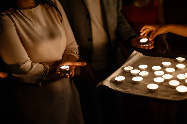 As pessoas têm uma vela nas mãos. Os empregados estão a distribuir as velas da bandeja. . — Fotografia de Stock