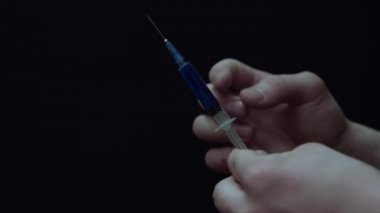 İçinde mavi bir sıvı ile şırınga dokunarak genç bir adam closeup, sonra havaya bazı sıvı Sprinkles. Siyah üzerinde izole. Uyuşturucu bağımlısı kavramı.