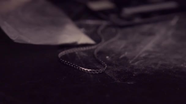 Une chaîne argentée est posée sur une table noire désordonnée à côté d'un portefeuille et d'un sac en plastique avec de la poudre blanche. Isolé sur noir .