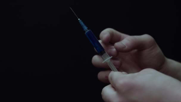 一个年轻人用蓝色液体敲击注射器的特写镜头 然后他将一些液体洒到空气中 在黑色上隔离 吸毒成瘾者的概念 — 图库视频影像