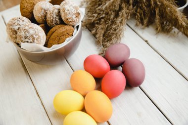 Kurabiyelerle dolu bir fincan beyaz bir masanın üzerinde bir demet yumurta ve biraz buğday dikeni duruyor..