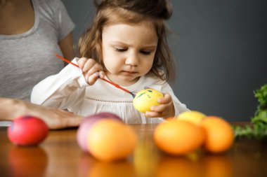 Genç bir kadın ve kızı birlikte vakit geçiriyorlar. Kız paskalya yumurtası çiziyor. Gri arka planda yalıtılmış.