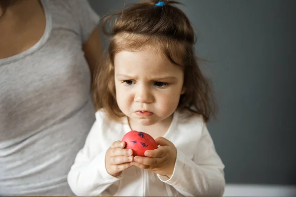 Upset young girl is holding a red easter egg with her hands. Bad taste concept.