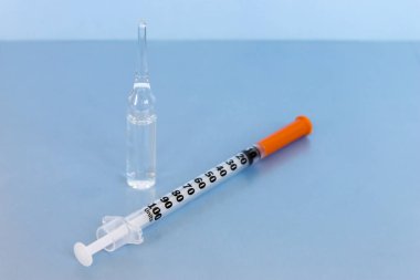 Şeffaf şişe konteyner sıvı ilaç yakınındaki küçük insülin şırınga üzerinde mavi arka plan ile. Aşı, subkutan yönetim için hazırlık kavramı