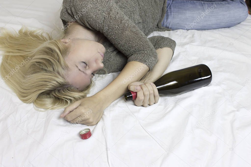 Young blond woman with alcohol bottle in the bed