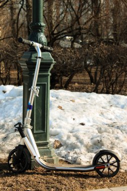Bahar sokak lâmbası direği City Park yakınındaki scooter ayakta tekme. Arka planda kar.