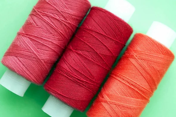 Three coils  of threads of red pink and orange shades of colors on mint vanilla green background close-up