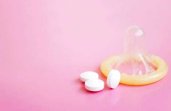 コピー スペースとコンドームとピンクの背景に白い錠剤を開く — ストック写真