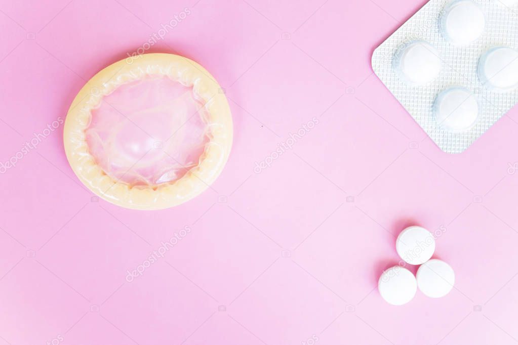 Opened condom and white pills fdn pills in blister on pink background with copy space