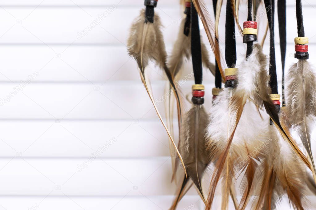 Dream catcher with feathers threads and beads rope hanging, white window blinds on background. Dreamcatcher handmade