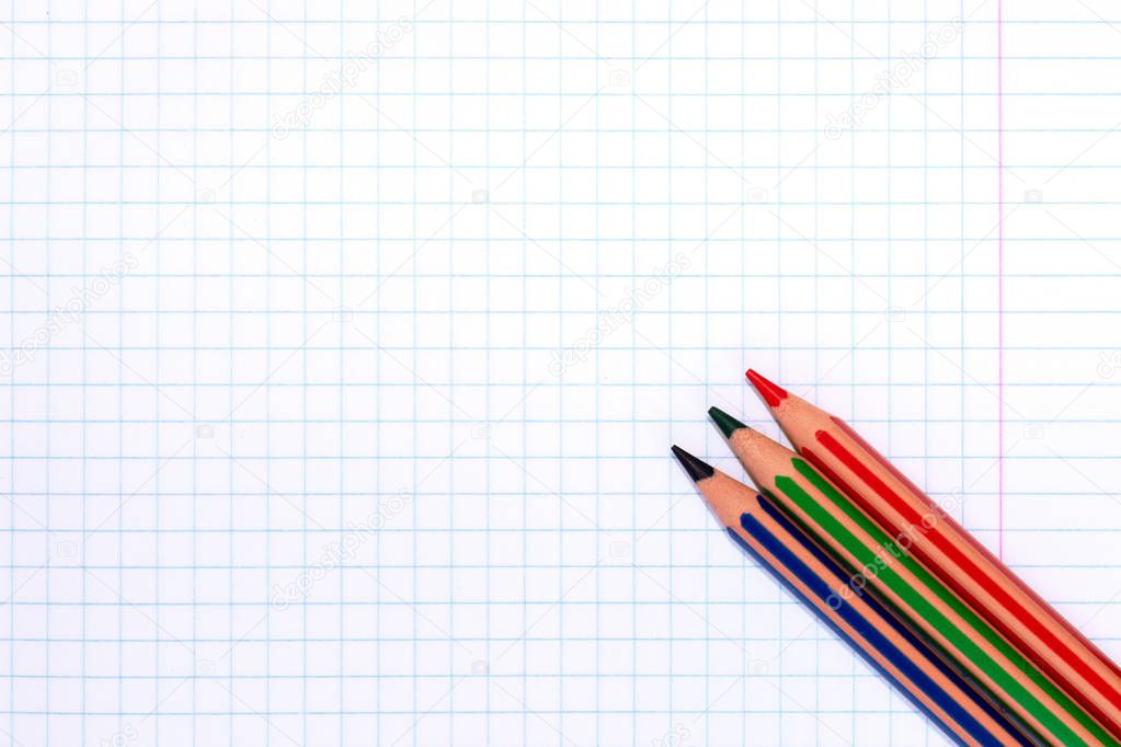 Colorful pencils of red, green and blue colors on a checkered exercise book paper with copy space.