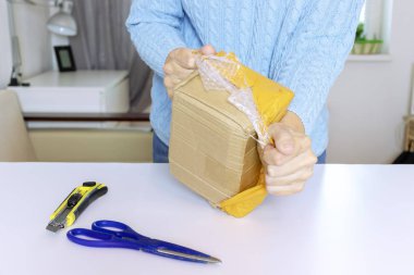A woman in blue pullover unpacks, unbox, tears the plastic packaging on the parcel. clipart