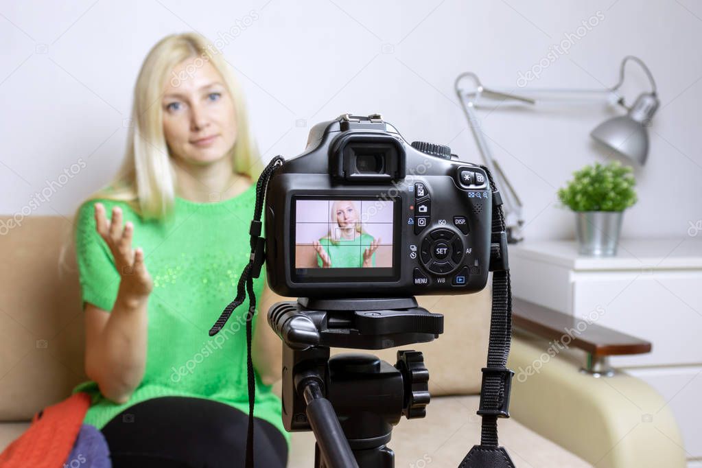 Close up photo of camera on tripod with young womanon LCD back screen and blurred scene on background. Female video blogger recording vlog or podcast, streaming online.
