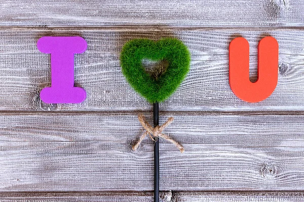 Sign I love you made of colorful letters and green grass heart on vintage wooden background, flat lay.