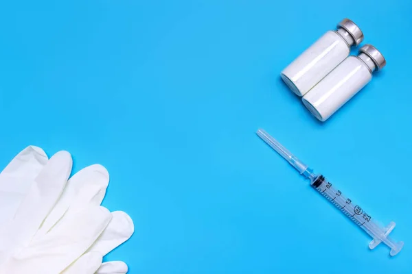 Medical gloves, syringe and vials on blue background with copy space, flat lay, top view.