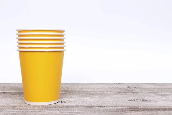 Stack of green paper disposable cups for coffee and nonalcoholic drinks on wooden background.