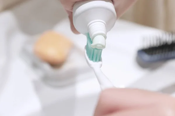 Cropped hands squeezed the toothpaste from the tube onto the brush, bathroom Interior.