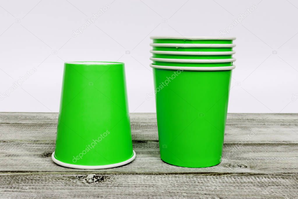 A stack of green take away disposable paper cups on wooden desk with white background.
