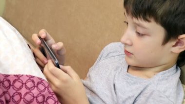 Bir çocuk kanepede oturan ve smartphone oyun