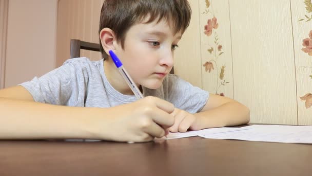 A fiú otthon az asztalnál ül, és írásban tollal papírra