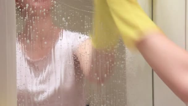 无法辨认的妇女在黄色橡胶手套洗浴室镜子与黄色擦拭和泡沫清洁剂 擦拭和清洗镜子的概念 — 图库视频影像