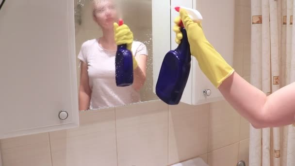 若い金髪女性バスルームの鏡を洗う黄色いゴム手袋でクリーナー ワイパー噴霧および泡と散水します 拭き取り 洗浄の概念をミラー化します — ストック動画