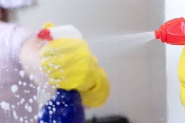 Temizlik püskürtülen ilaç şişe ve cam ayna yüzeyi serpin mavi tutan sarı lastik eldiven El. Yıkama, temizleme ve kavram silme