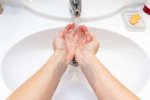 A woman wishing hands with water in bathroom sink. Desease prevention and hygiene concept. Useful, good habit.
