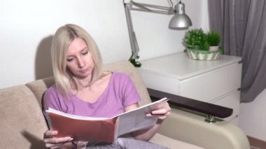 Kanepede oturan ve klasör leafing genç sarışın kadın