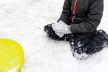 Yedi yaşında kar ve ona yalan bir yeşil plastik daire kızak üzerinde oturan bir çocuk. Kış aktiviteleri, rekreasyon ve çocuk eğlence kavramı.