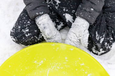 Yedi yaşında kar ve ona yalan bir yeşil plastik daire kızak üzerinde oturan bir çocuk. Kış aktiviteleri, rekreasyon ve çocuk eğlence kavramı.