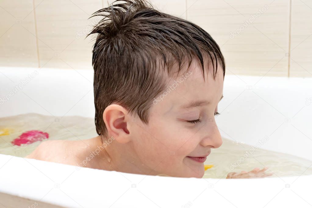 An eight year old boy sitting in bath and swimming.