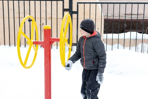 Street workout equipment in winter, outdoor sport fitness and bodybuilding. Boy in a sport playground.