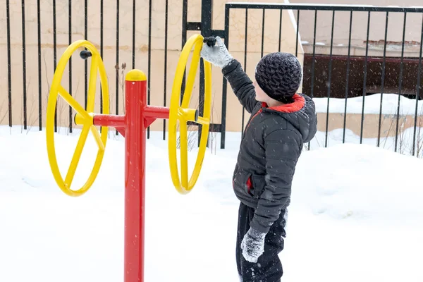 Street workout equipment in winter, outdoor sport fitness and bodybuilding. Boy in a sport playground.