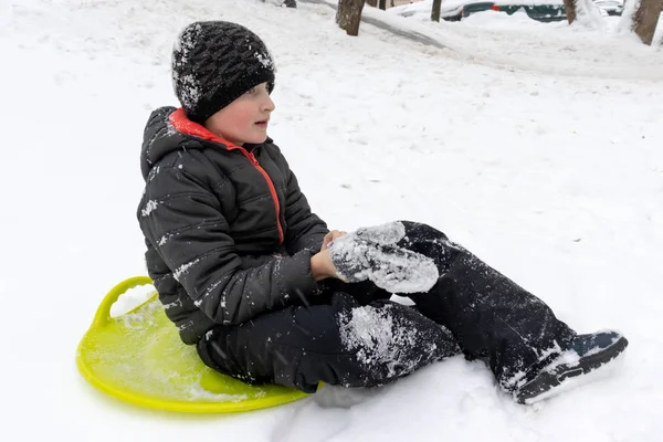 Yedi yaşında bir yeşil plastik daire kızak bir slayt binmeye hazır oturan eski bir çocuk. Kış aktiviteleri, rekreasyon ve çocuk eğlence kavramı.