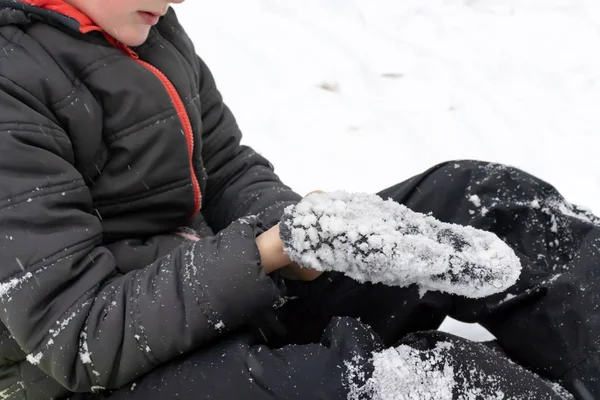 Yeşil plastik daire kızak üzerinde oturan ve onun mittens tüm karda koyarak yedi yaşında bir çocuk. Kış aktiviteleri, rekreasyon ve çocuk eğlence kavramı.