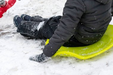 Yedi yaşında bir çocuk ile slayt, yeşil buz kızak üstünde belgili tanımlık tepe aşağı gidiyor. Kış aktiviteleri, rekreasyon ve çocuk eğlence kavramı.