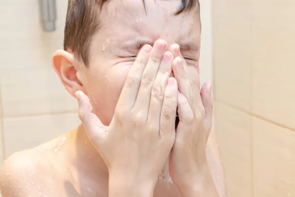 A preteen boy wiping his face with hands after shower or bath.