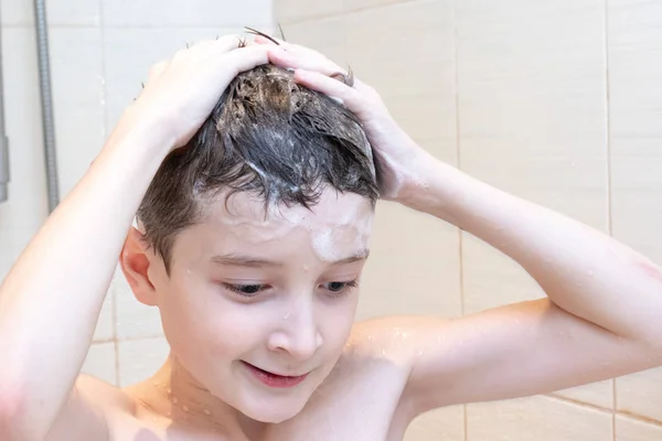 Hygienic procedures and healthy habits of a preteen boy - taking shower and washing hair with shampoo.